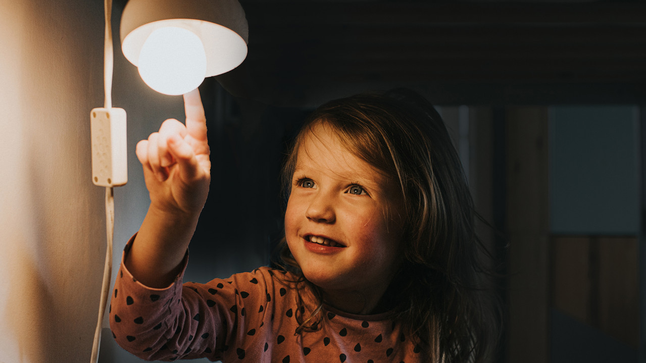 A child in the dark is happy about a glowing light bulb that it touches.