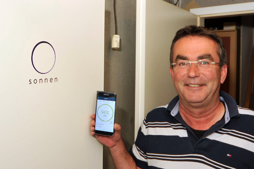 sonneBatterie Kunde vor seinem Stromspeicher mit Handy auf dem sie monitoring App ge&ouml;ffnet ist