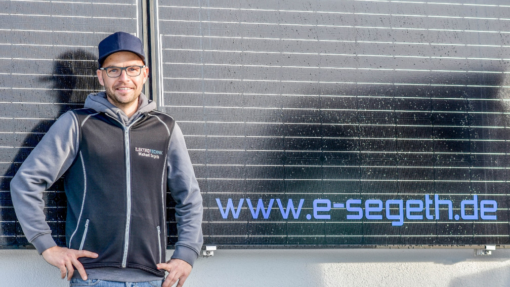 Michael Segeth vor dem Betriebsgeb&auml;ude und dem Logo im Hintergrund.